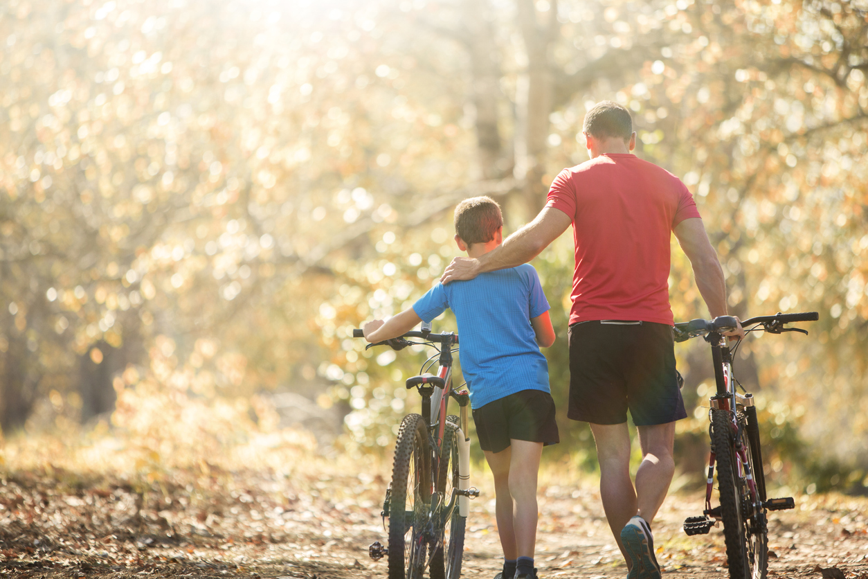 Affectionate father and son walking mountain bikes on path in woods Affectionate father and son walking mountain bikes on path in woods
